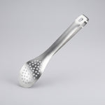 Hand holding a metal spatula over a piece of bread on a black surface with a strawberry and other items.